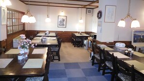 Un restaurante con mesas y sillas de madera, lámparas colgantes y cuadros en las paredes.