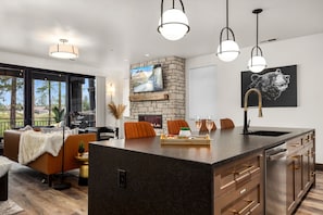 A modern kitchen with a large island, stone fireplace, and a dining area with a view.
