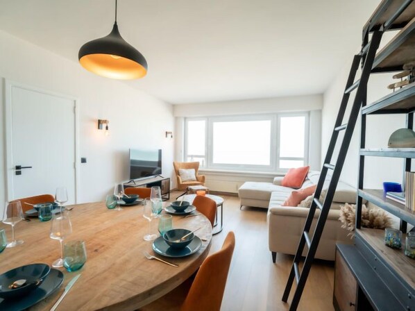 A modern living room with a wooden dining table set for a meal, a sofa, a TV, and a bookshelf.