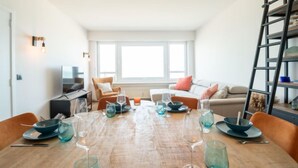 A modern living room with a wooden dining table set for a meal, a sofa, a TV, and a bookshelf. - Escape with sea view by Interhome (Blankenberge)