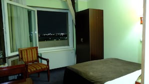 A hotel room with a bed, a chair, a wardrobe, and a window with a view of the city at night. - Grand Bukhara (Bukhara)