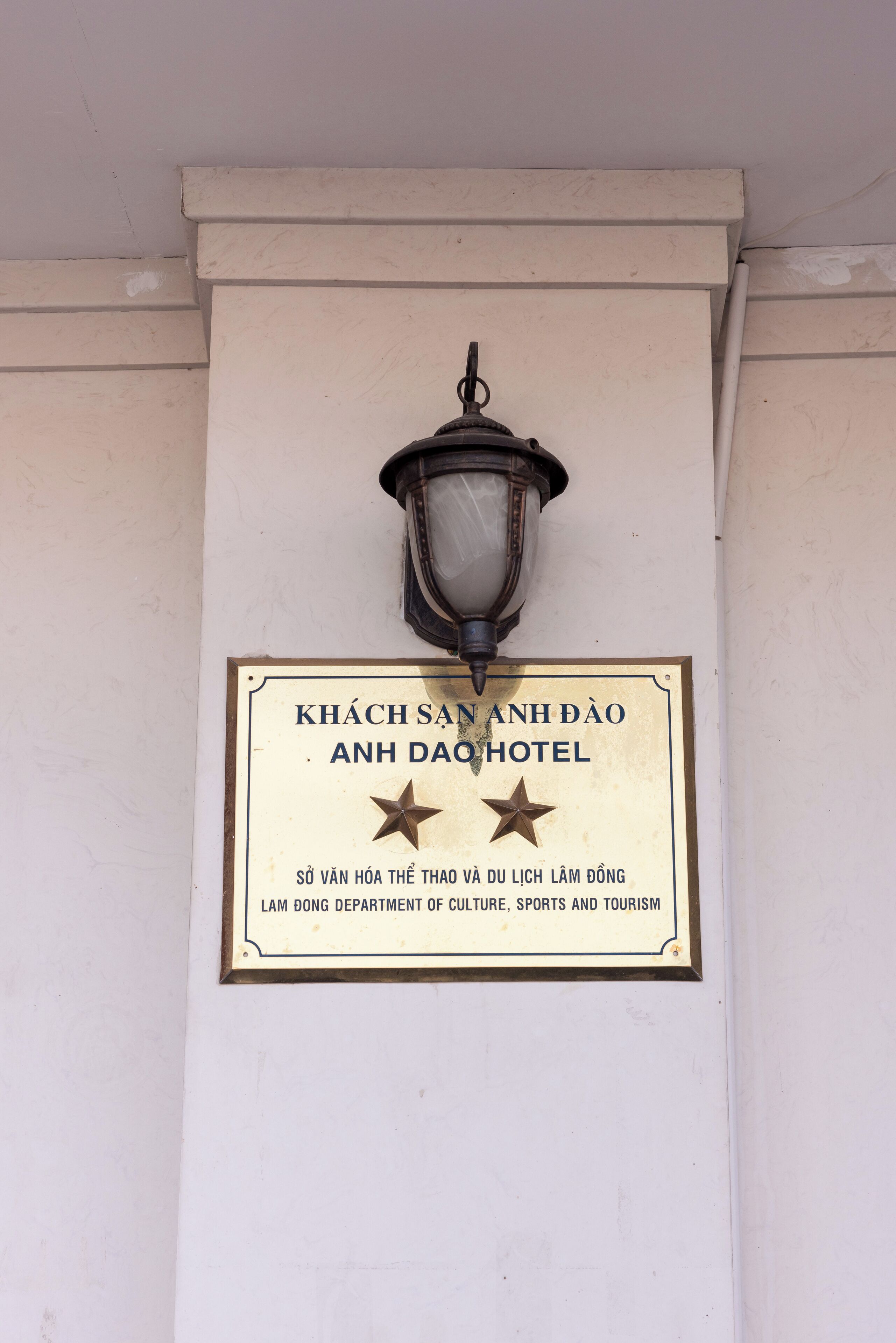A sign for Khách sạn Anh Dạ Hotel, indicating it is managed by the Lam Dong Department of Culture, Sports, and Tourism.