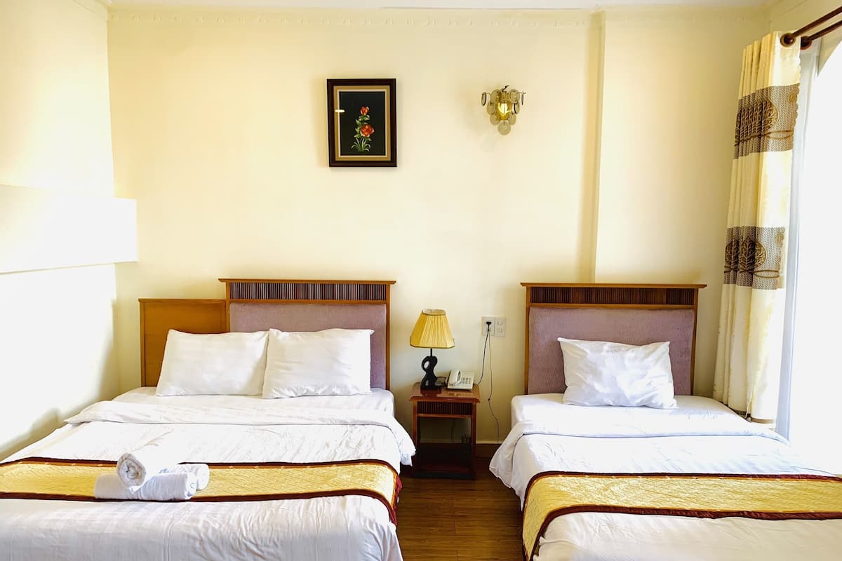 Two single beds with wooden headboards and white bedding, a bedside table with a lamp and telephone, and a framed picture adorn this cozy space.