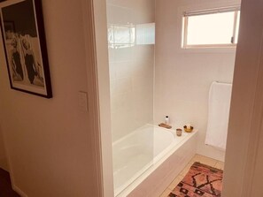 Ein Badezimmer mit einer Badewanne, einem kleinen Fenster und einem gefliesten Boden.