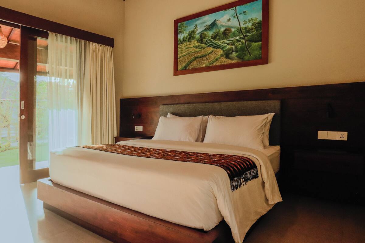 A bedroom with a large bed, a wooden headboard, and a painting of a landscape on the wall.