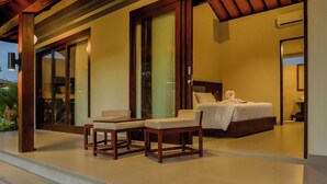 Habitación de hotel moderna con una cama grande, un área de descanso con dos sillones y un balcón con vistas al jardín.