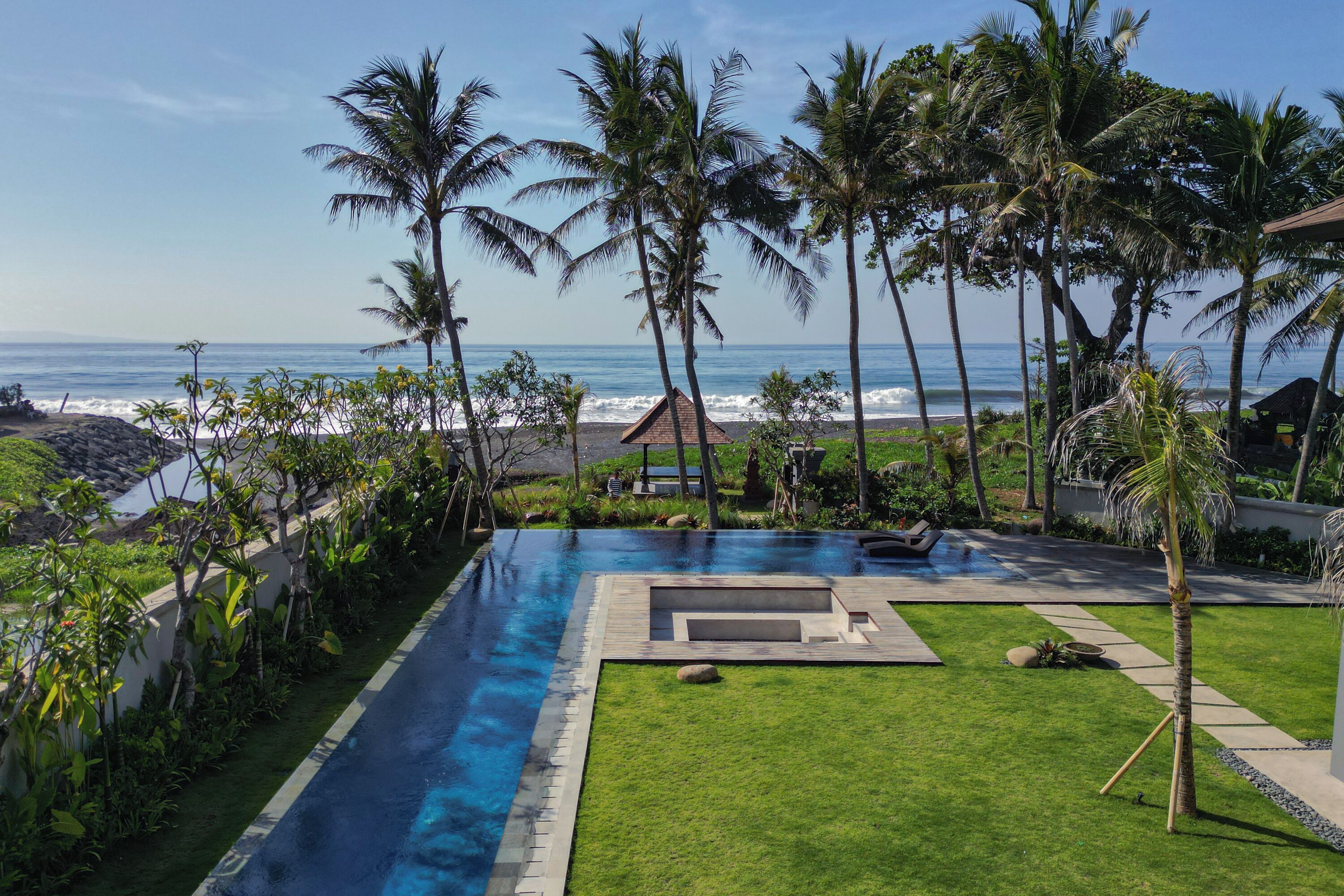 A swimming pool with a view of the ocean, surrounded by palm trees and a small building.