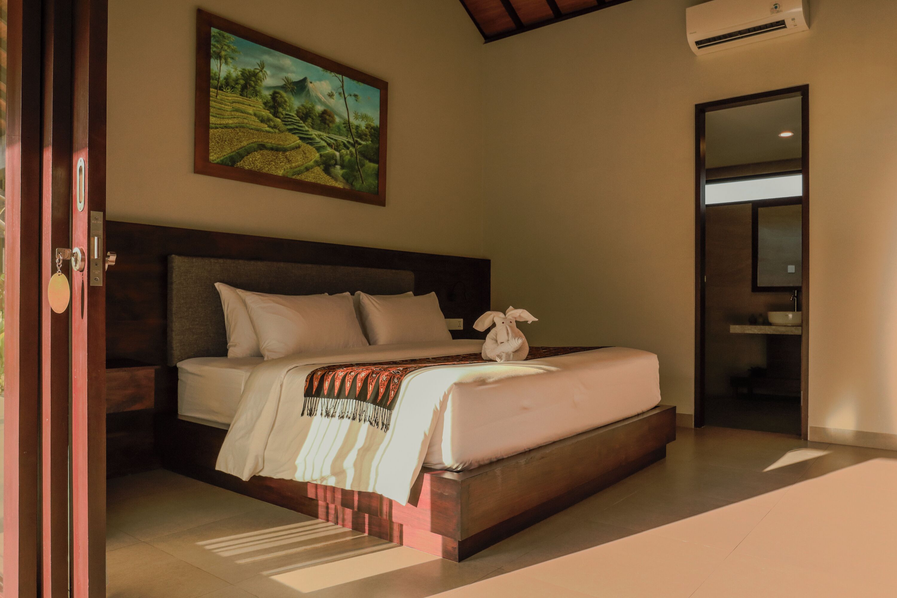 Een slaapkamer met een groot bed, een schilderij aan de muur en een badkamer die door een open deur zichtbaar is.
