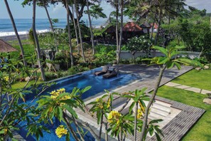 A swimming pool with a wooden deck, surrounded by tropical vegetation and overlooking the ocean.
