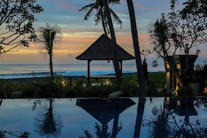 A beachside view with a wooden structure, palm trees, and a reflective pool. - K Ko Surf Village (Gianyar)