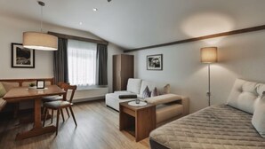 A modern hotel room with a wooden dining table, a sofa, a bed, and a small table with a lamp.