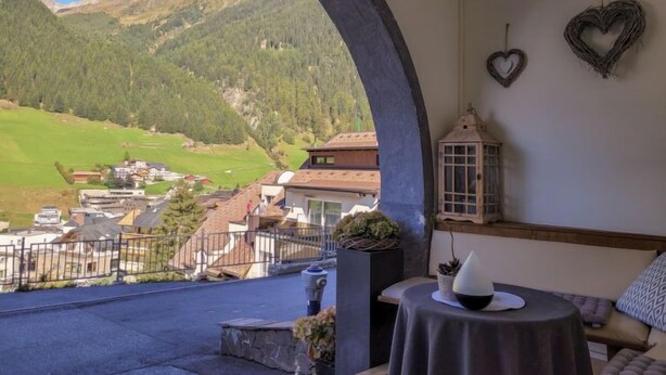 Una habitación con vista a un valle y montañas, una mesita con un florero, y dos adornos con forma de corazón en la pared.