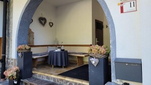 Un área de estar al aire libre con techo, un banco de piedra, una mesa con mantel y adornos con forma de corazón en la pared.
