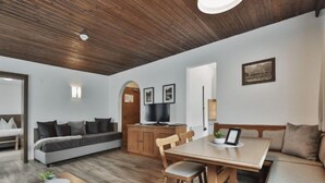En moderne stue med træloft, sofa, spisebord med stole og fjernsyn.