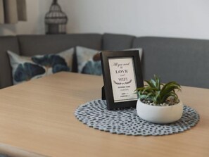 Uma placa emoldurada com mensagem sobre amor e WiFi, colocada sobre uma mesa de madeira com um jogo americano e uma planta em vaso.