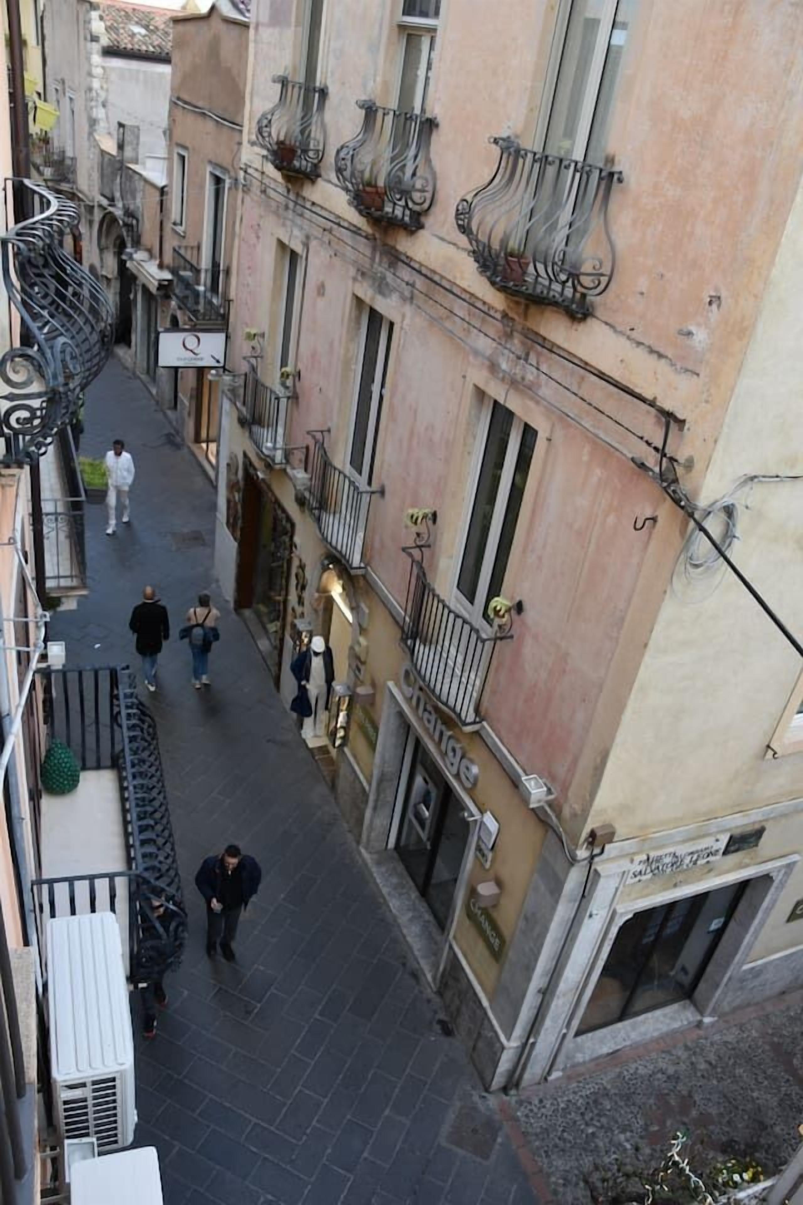 Una calle estrecha en la ciudad, con edificios, balcones y algunos peatones.