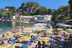 Une plage avec de nombreuses chaises longues et des parasols, une côte rocheuse et des bâtiments en arrière-plan.