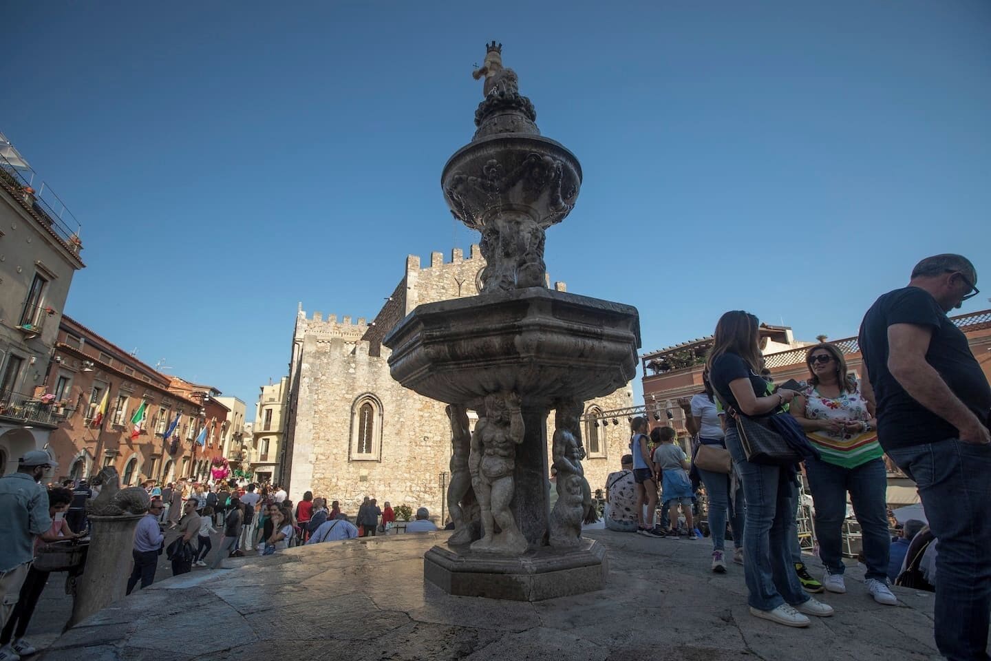 A historic fountain in a public square with stone buildings in the background.