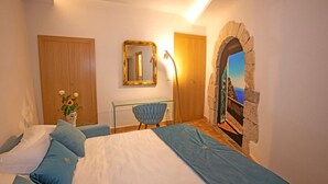 Un dormitorio con cama, una silla, un espejo, un arco de piedra y vista al mar.