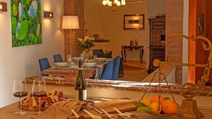 Un comedor con una mesa lista para dos personas, una botella de vino y una cesta de fruta.