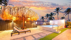 Uma área de piscina com estrutura de palha, espreguiçadeiras e hidromassagem.