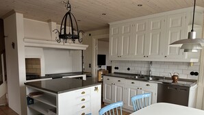 Una cocina con armarios blancos, una estufa y un lavabo. Hay sillas azules y una mesa blanca.