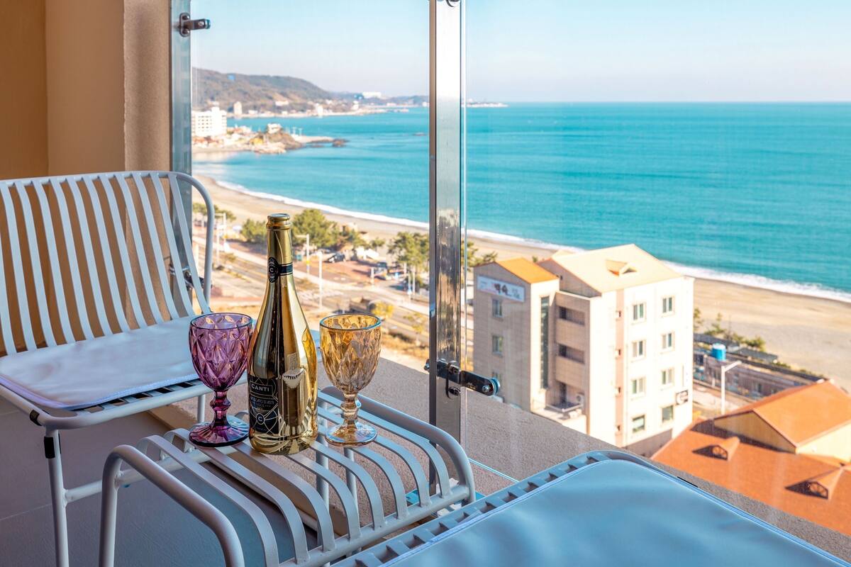 A balcony with a view of the beach and ocean, a bottle, and two glasses on a table.
