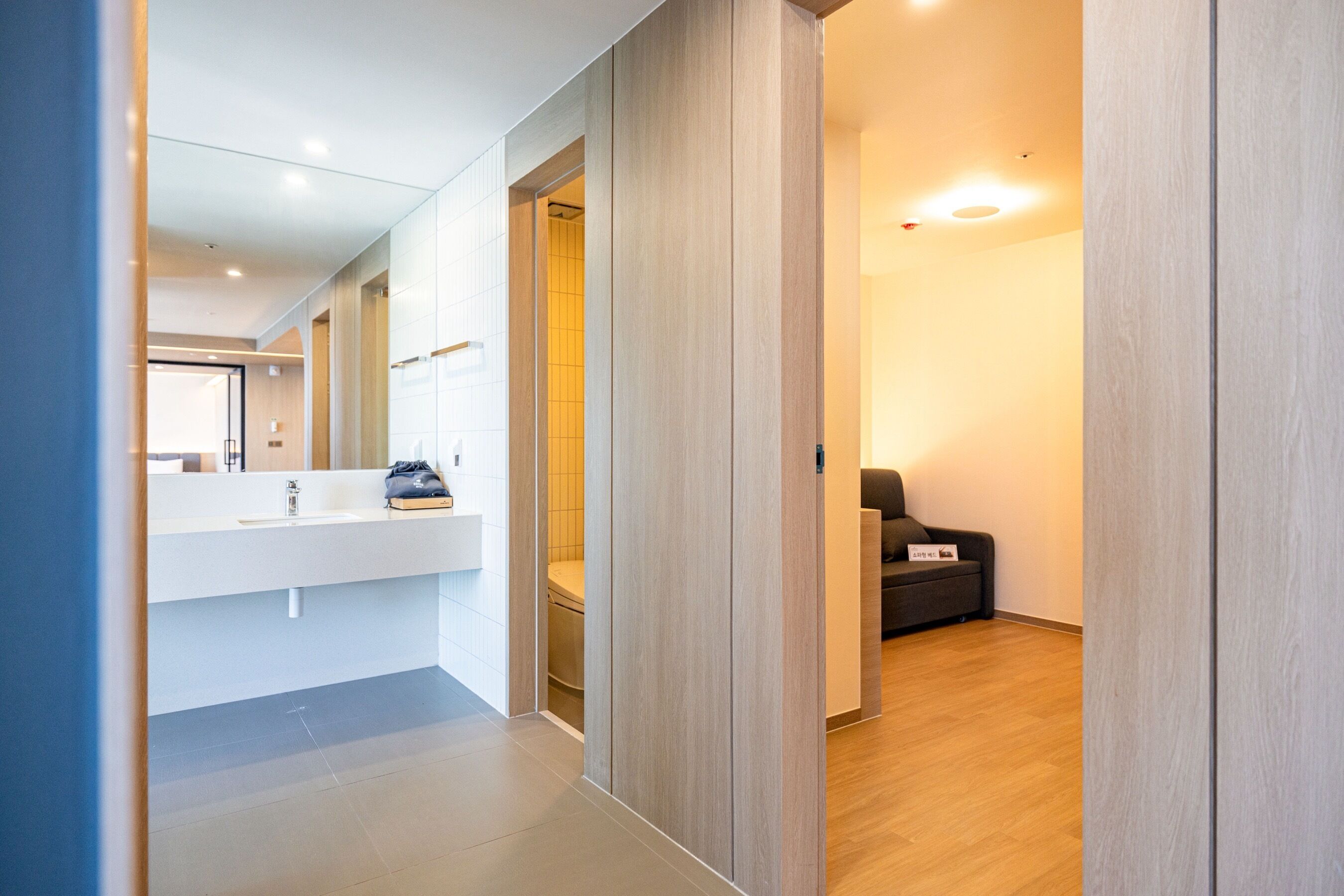 A modern bathroom with a large mirror, a white sink, and a wooden floor.