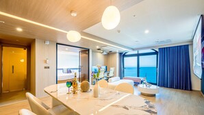 A modern hotel room with a marble dining table, comfortable seating, a large window with a view of the sea, and a balcony with a view of the ocean. - Hound Hotel Ulsan (Ulsan)
