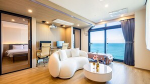 A modern interior with a curved white sofa, a round coffee table, and a view of the sea through large windows. - Hound Hotel Ulsan (Ulsan)