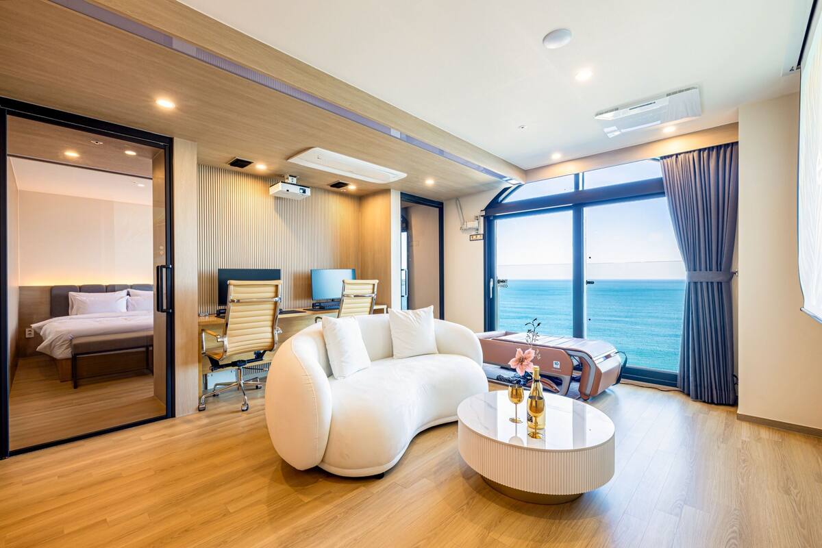 A modern interior with a curved white sofa, a round coffee table, and a view of the sea through large windows.