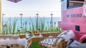A pink bus with "HOUND" written on it, parked by a seaside with a table and chairs under an umbrella. - Hound Hotel Ulsan (Ulsan)