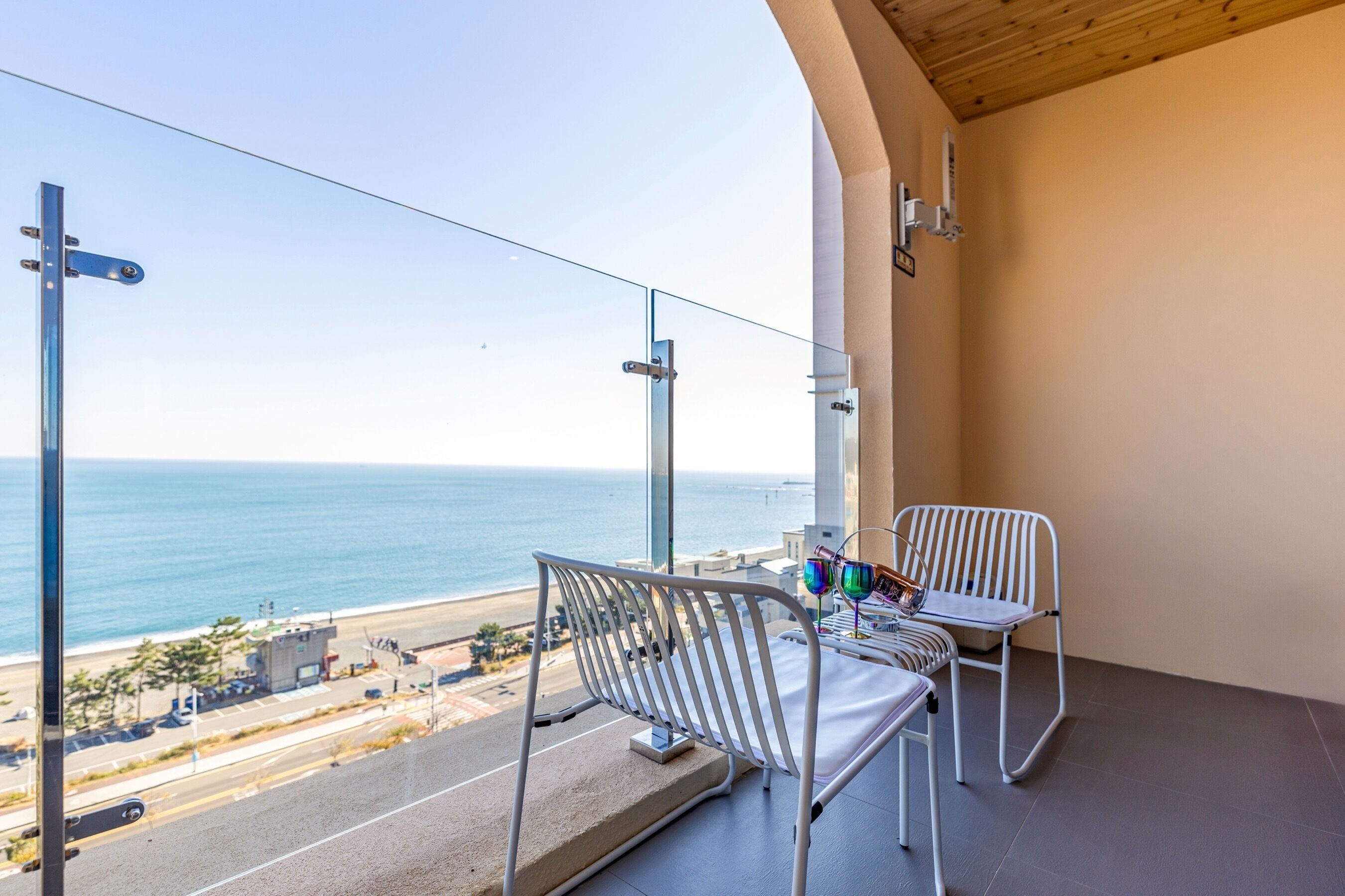 A balcony with two white chairs and a table, overlooking a beach and ocean.