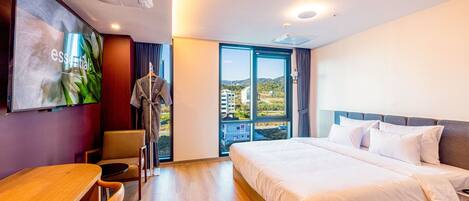 Habitación de hotel moderna con una cama grande, un escritorio y vistas de la ciudad a través de un ventanal.