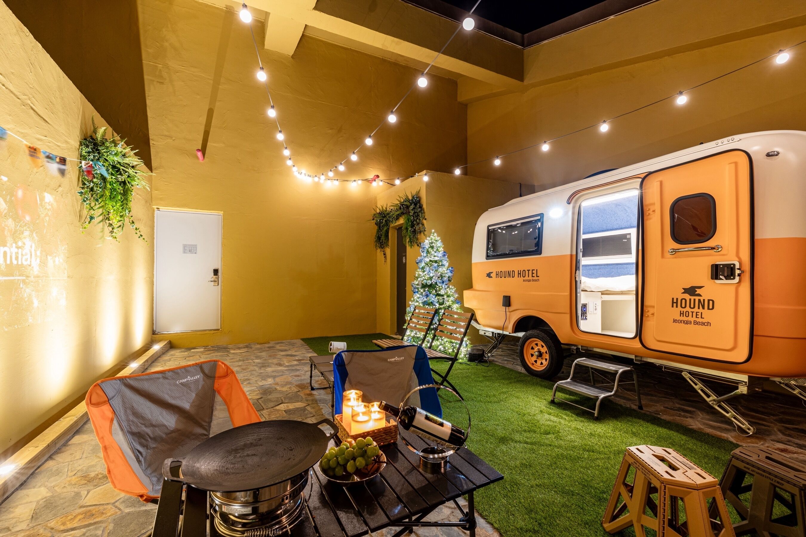 Un espacio interior acogedor con una mesa de comedor, sillas, un pequeño árbol de Navidad y una autocaravana con la leyenda "HOUND HOTEL Jeonju Beach".