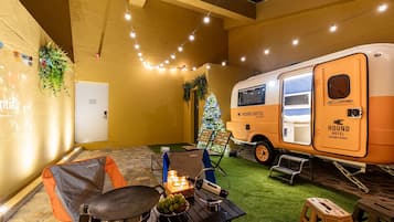 Un espacio interior acogedor con una mesa de comedor, sillas, un pequeño árbol de Navidad y una autocaravana con la leyenda "HOUND HOTEL Jeonju Beach".