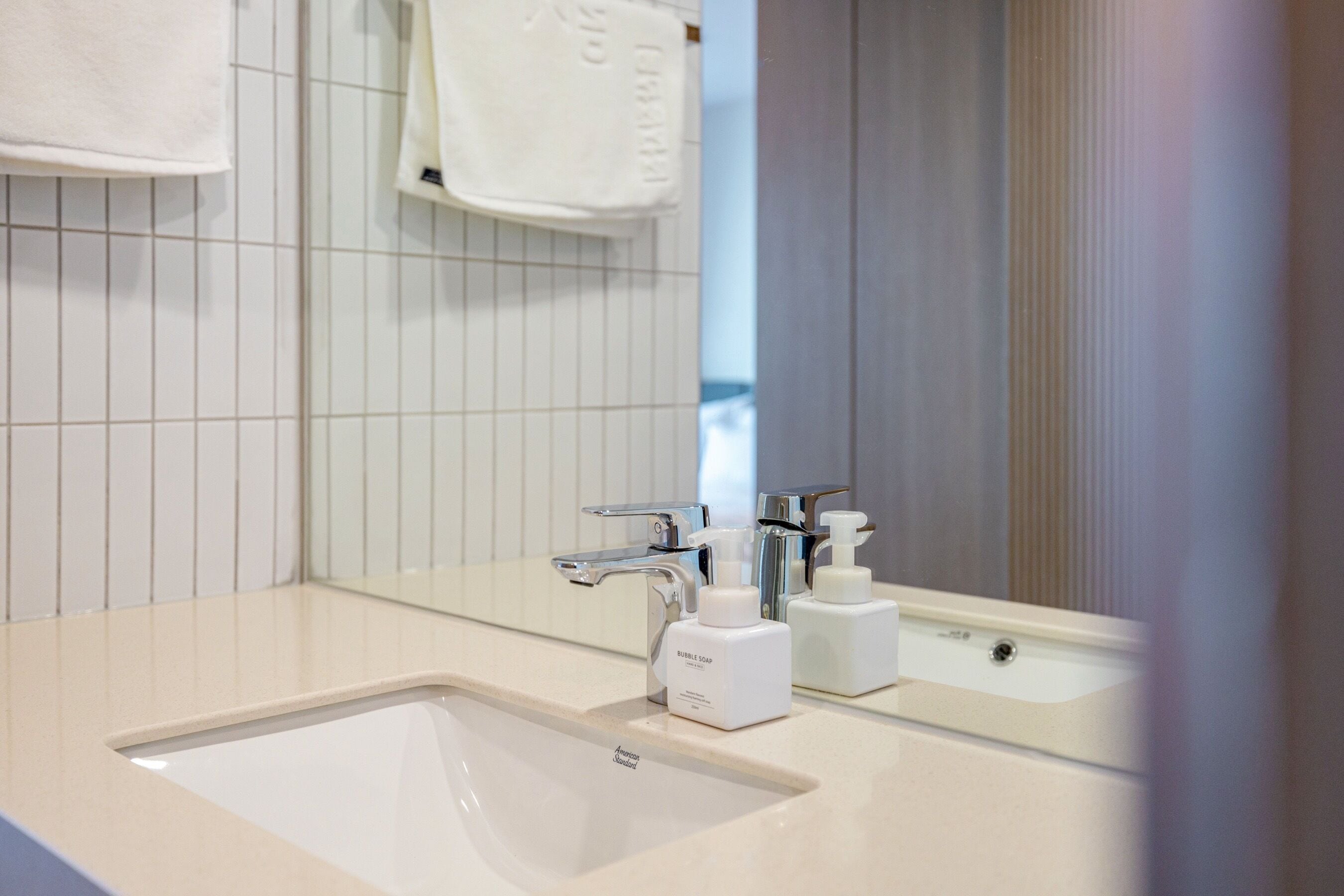 A bathroom with a white sink, chrome faucet, and a mirror reflecting a towel and a bottle of soap.