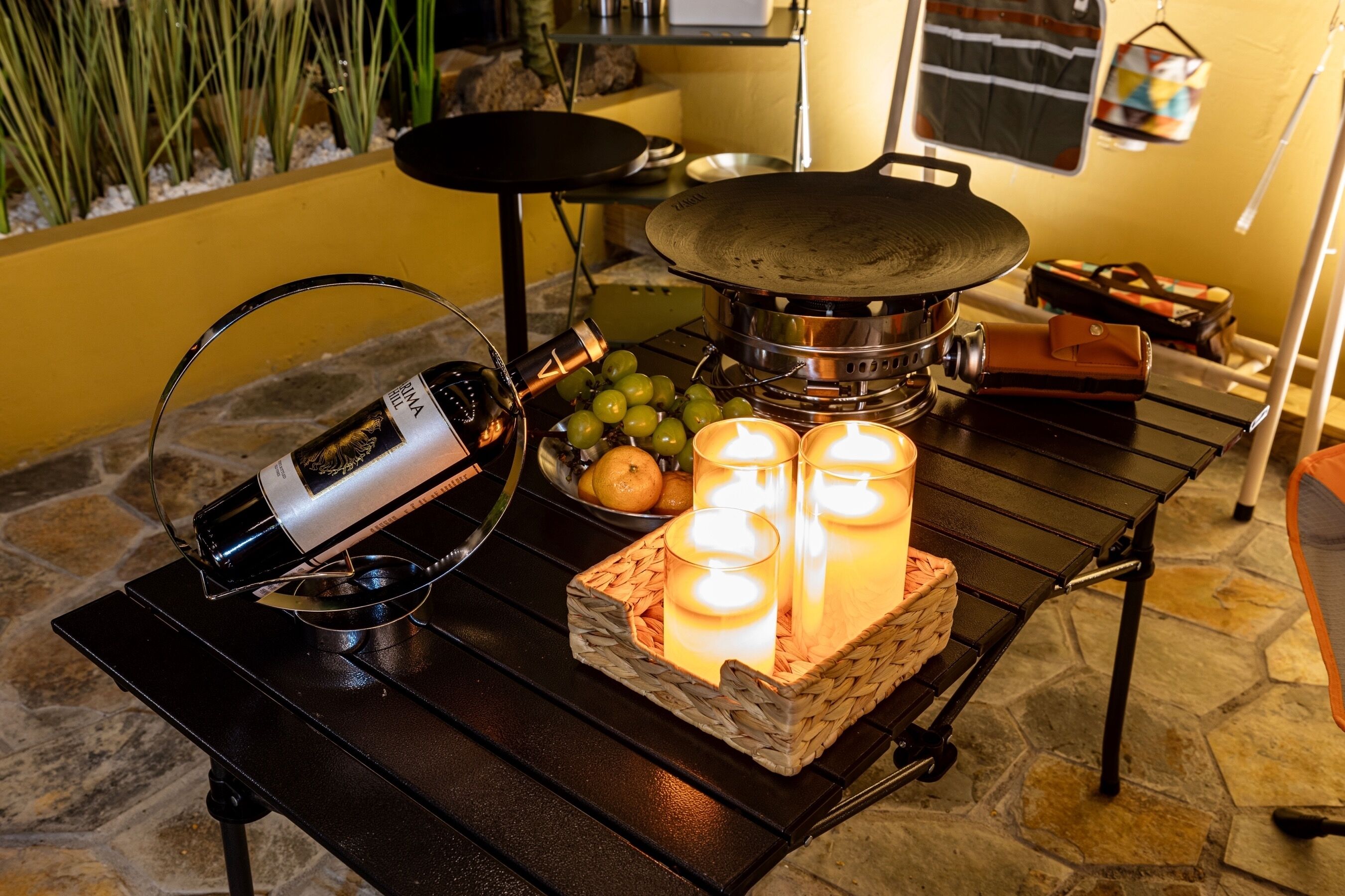 A table with a bottle, grapes, candles, and a portable stove.