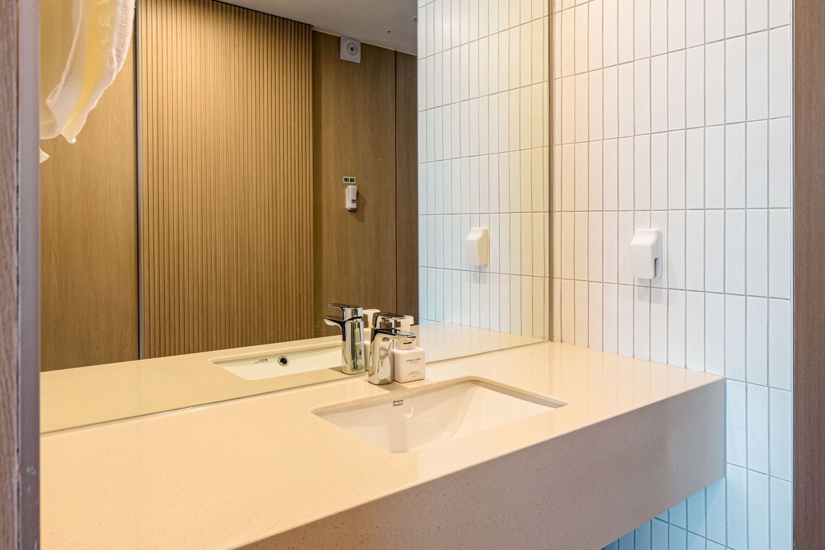 Un baño moderno con un lavabo color beige, un espejo y un revestimiento de pared de madera.