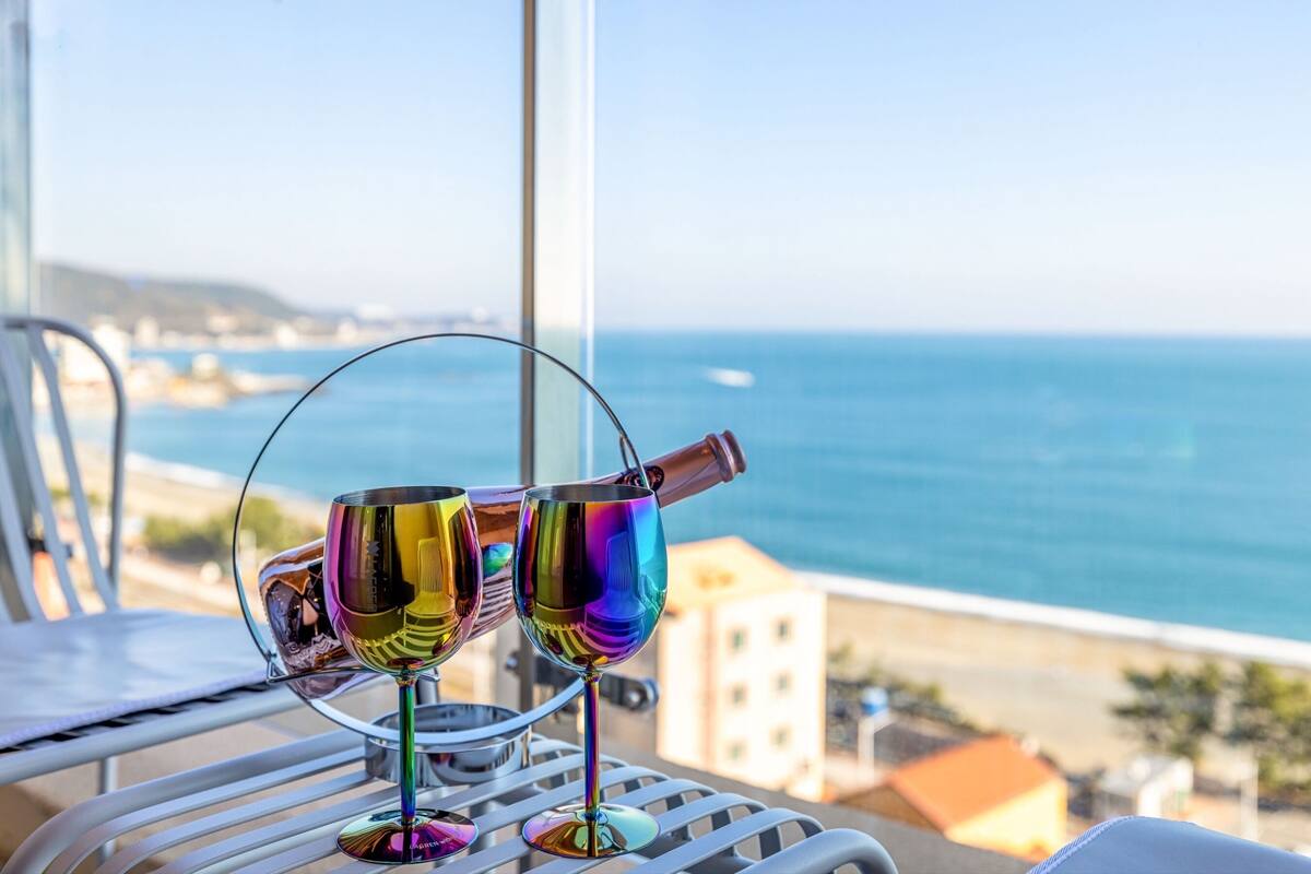 Two wine glasses on a balcony with a view of the sea.