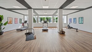 A spacious indoor gym with exercise equipment, large windows, and artwork on the walls. - Home and Coliving Bonn Aparthotel (Bonn)