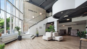 A spacious lobby with a staircase, a sofa area, and large windows. - Home and Coliving Bonn Aparthotel (Bonn)