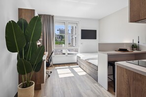 Cozy living space with a large window, comfortable bed, and a small desk area.