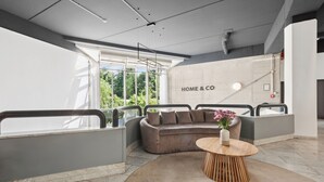 A modern interior with a grey sofa, a round wooden table, and a large window with a view of greenery. - Home and Coliving Bonn Aparthotel (Bonn)