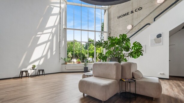 A modern living room with a large window, wooden flooring, and a sofa. - Home and Coliving Bonn Aparthotel (Bonn)