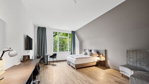 A modern bedroom with a bed, a desk, a chair, a sofa, and a TV. - Home and Coliving Bonn Aparthotel (Bonn)