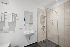 A modern bathroom with a glass-enclosed shower, a white sink, and a mirror above it. - Home and Coliving Bonn Aparthotel (Bonn)