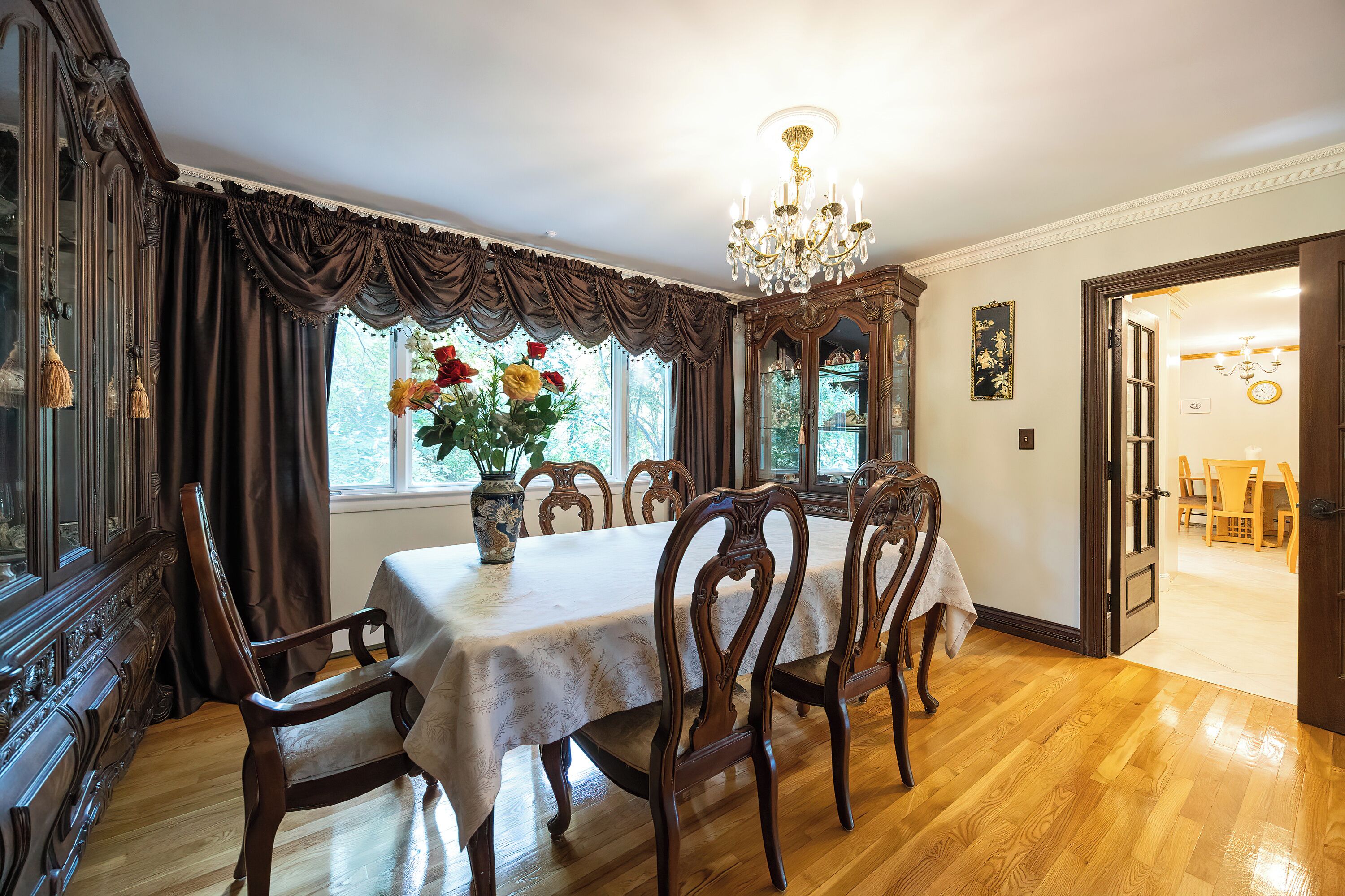 Una sala da pranzo con un tavolo in legno, sedie, un lampadario e una finestra con tende.