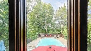En swimmingpool med en rød parasol, omgivet af et træterrasse og et hegn.