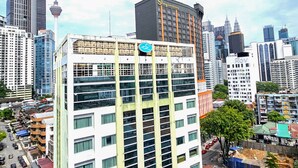A multi-story hotel with a prominent sign on the top, surrounded by high-rise buildings and a clear sky.